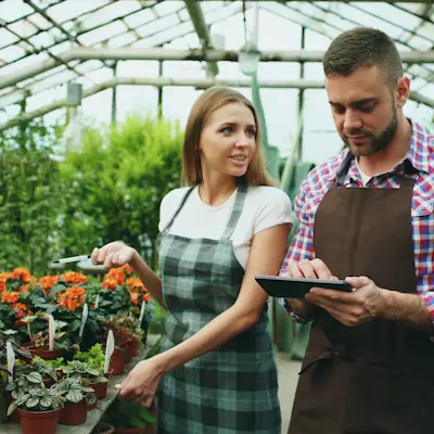 Man and woman in greenhouse reviewing tablet for landscaping business and customer follow-up.
